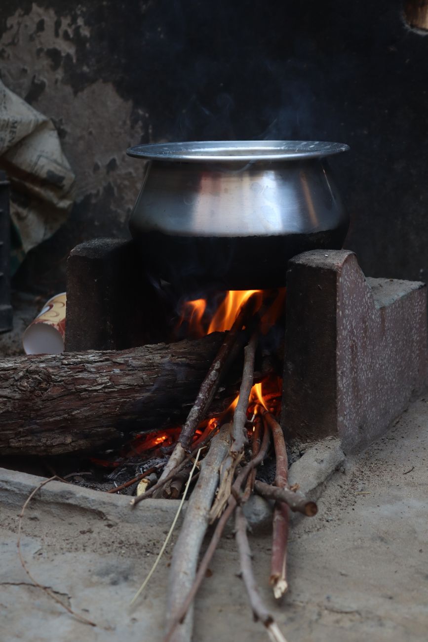 A traditional stove with a metal pot over an open fire fueled by wood logs outdoors.