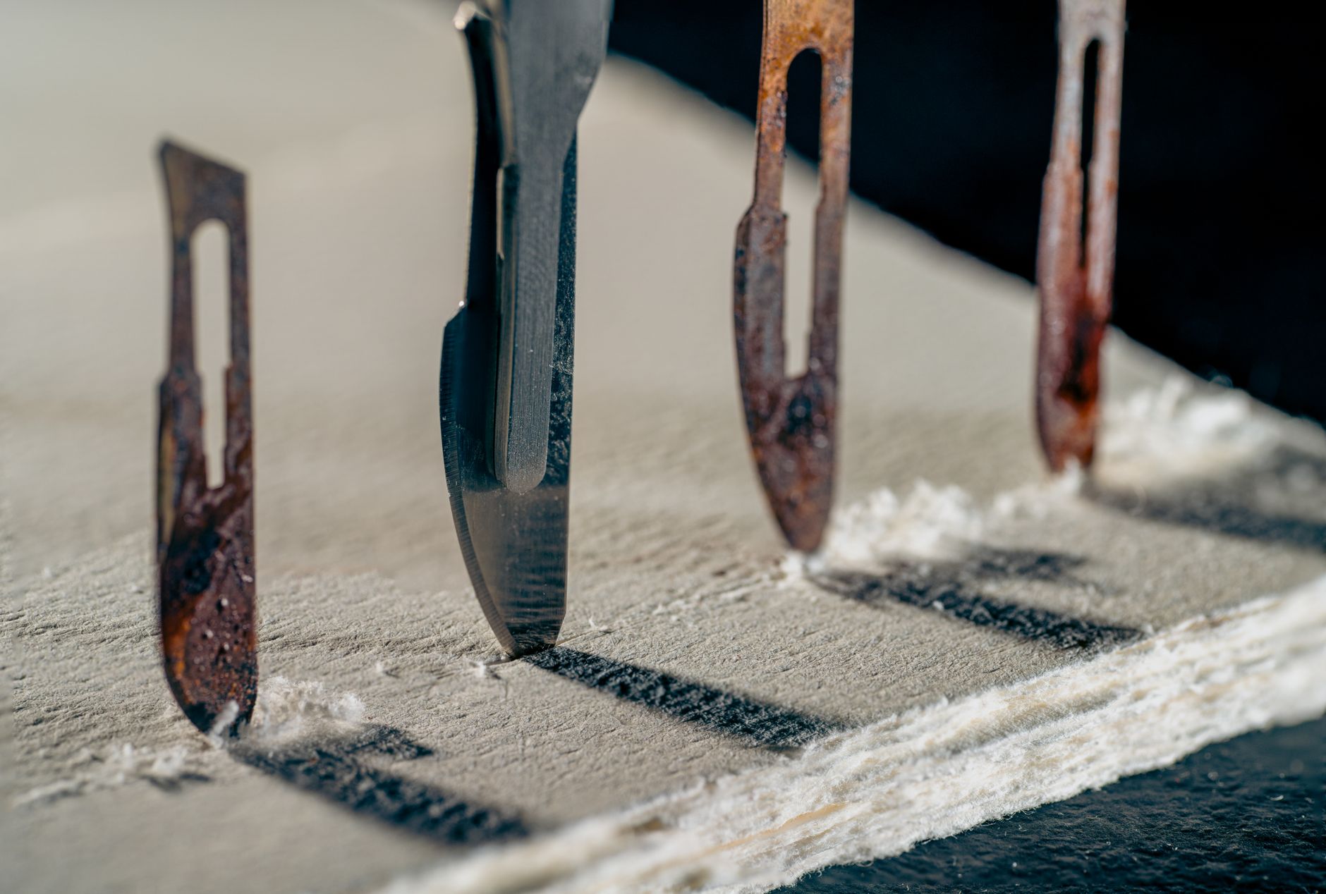 Detailed view of old and rusty scalpel blades lined up on a textured surface casting shadows.