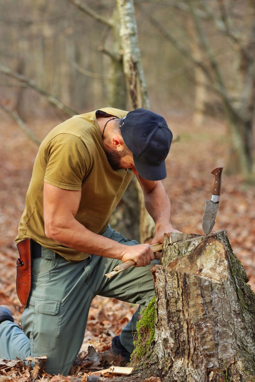 Man carving wood in an autumn forest, showcasing outdoor skills and survival techniques.